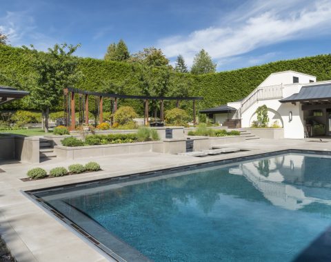 A tiered stone water feature with matching pool tile accents serves as a striking focal point, while a long bench, rich blue plaster, a sleek modern tile band, and an automatic cover complete this contemporary pool’s seamless blend of style and luxury.