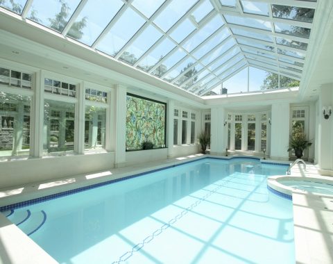 Indoor swimming pool builders have created an indoor pool surrounded by windows with a separate built in spa