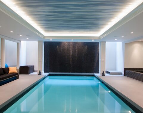 Indoor swimming pool builders have created a a pool with a stand out water feature wall