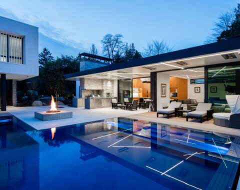 As night falls, the dynamic shapes of the flood edge pool—its curves and crisp angles—take on a new allure, accented by the pool’s deep blue plaster and elegant grey tile band.