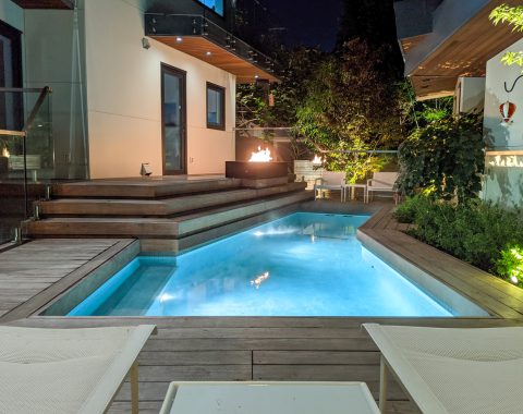 Pool view of a relaxing poolside with pool water features, lighting, and a stunning night scene.