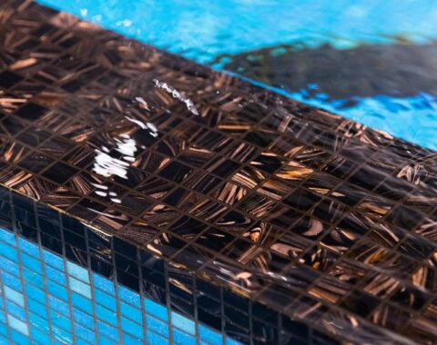 Up close photo of the rich chocolate color tile that is flecked with bronze to create an opulent look; a complemented contrast to the vibrant blue glass tile.