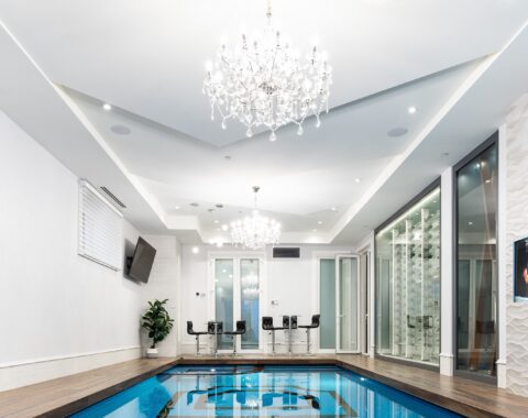 Luxurious indoor swimming pool with an elegant glass tile design, a built-in hot tub, and a stunning poolside view.