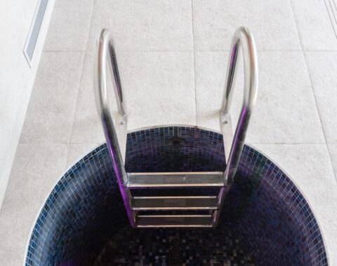 Cold plunge pool featuring a dark blue mosaic tile, a stark contrast to the bright white tones of the deck floor.