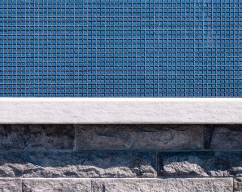 Up close photo of the 1x1 glass tile in a stunning vibrant blue that lines the infinity pool edge. A beautiful contrast to the neutral tones of the stones below.