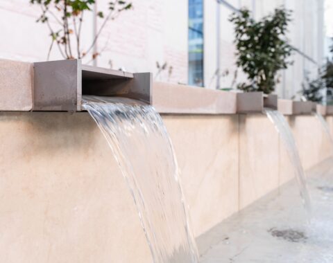 Waterfall feature with a sleek design, surrounded by contemporary architectural elements and landscaped greenery, exuding a tranquil atmosphere with soothing sounds and a peaceful ambiance.